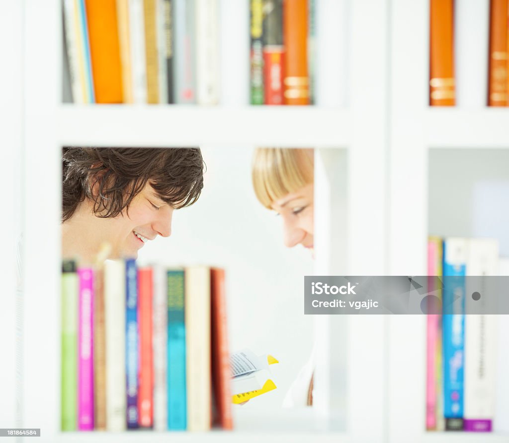 Adult Students in a library. Portrait of an young couple reading book in a library. Shot through book shelfs. Bookshelf Stock Photo