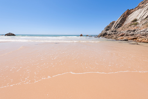 Clear blue sky, steep cliffs and the Atlantic Ocean viewed from a spot near Guincho Beach, Cascais and Lisbon in Portugal on a sunny day in summer. The image was captured with a full frame DSLR camera and a sharp wide-angle lens at low ISO.