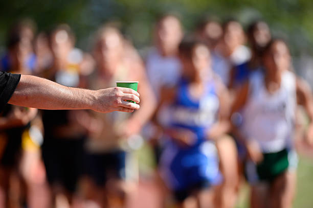 Arm holding out cup of water to marathon runners stock photo