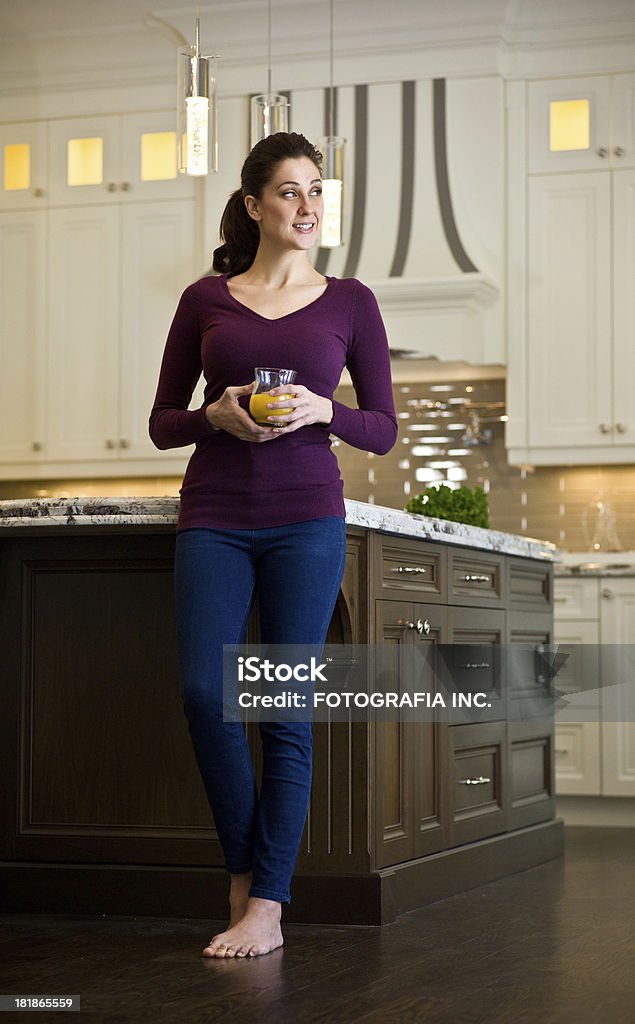 Young woman in the kitchen Young Caucasian woman enjoying a glass of orange juice in her new new luxury kitchen. Adult Stock Photo