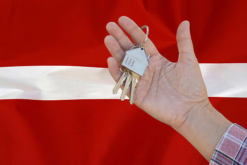 Keys to the apartment in a female hand on background of flag Latvia