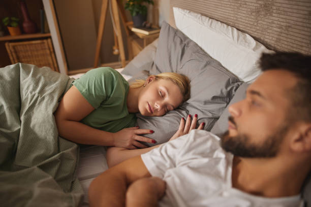 istock Sad man sitting in bed with female partner sleeping in background 1818683561