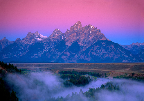 Beautiful magenta and blue sky highlight the Teton mountain. Fog is rising from the ground to make the scene more alluring.