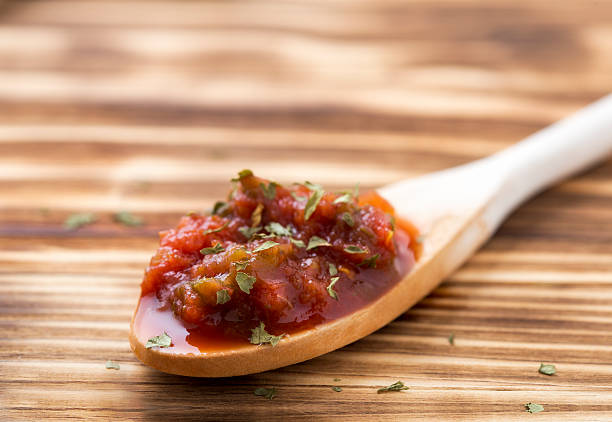 A wooden spoonful of tomato relish on a wooden board