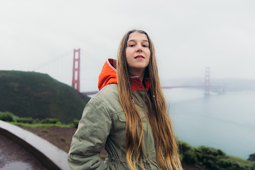 Side View of female traveller with long hair walking at the observation point of big red bridge during rainy spring calmness morning in San Francisco, the United States
