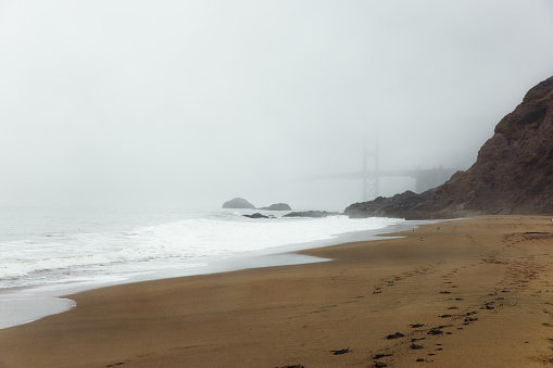 Dramatic view of tranquil scene at the beautiful central sand beach with red bridge covered by spring mist in San Francisco city, California