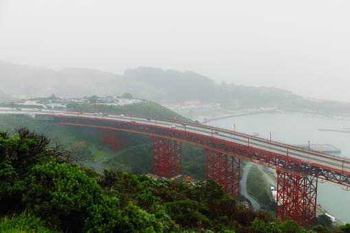 Dramatic photo of cars driving big red bridge above Pacific Ocean during spring cloudy morning in San Francisco city, the United States