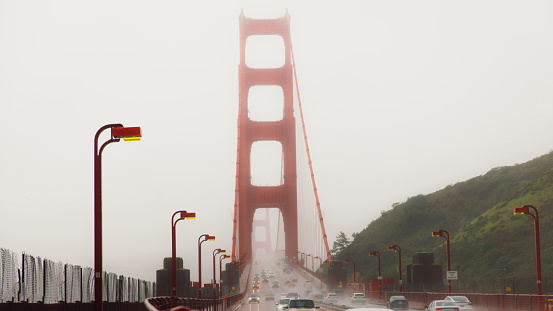 Dramatic photo of cars driving big red bridge above Pacific Ocean during spring cloudy morning with flowers in San Francisco city, the United States