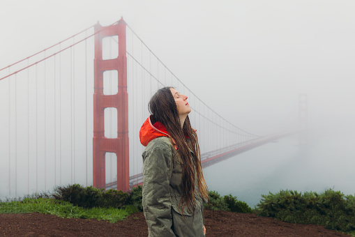 Side View of female traveller with long hair walking at the observation point of big red bridge during rainy spring calmness morning in San Francisco, the United States