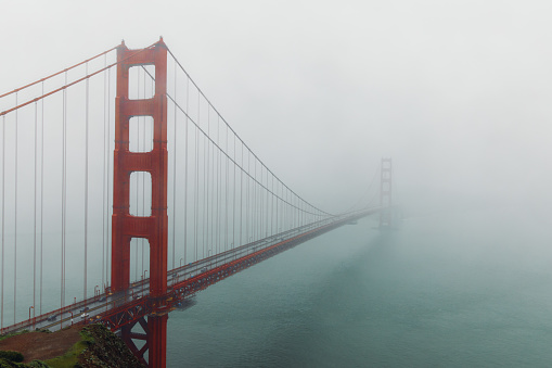 Dramatic photo of cars driving big red bridge above Pacific Ocean during spring cloudy morning in San Francisco city, the United States