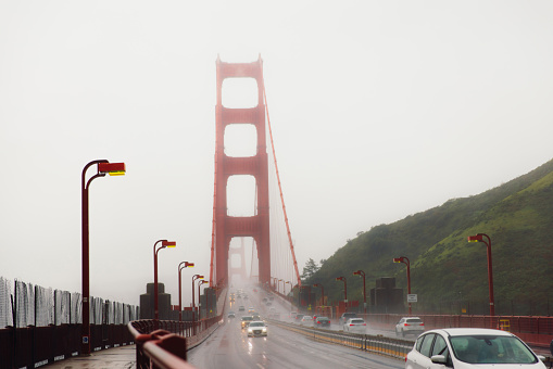 Dramatic photo of cars driving big red bridge above Pacific Ocean during spring cloudy morning with flowers in San Francisco city, the United States