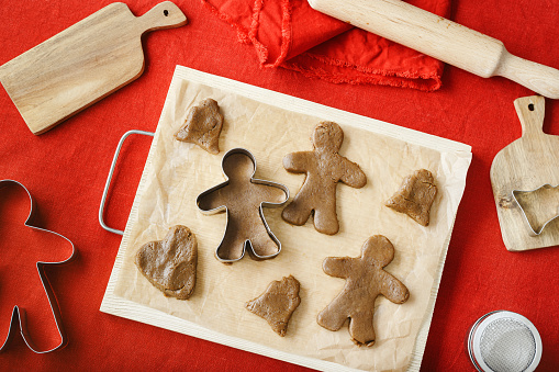 Top view preparing Cooking ginger cookies, Christmas and New Year traditional cookies in shape of gingerbread mans and bells, raw rolled out dough, metal pastry cutter on dough, wooden rolling pin