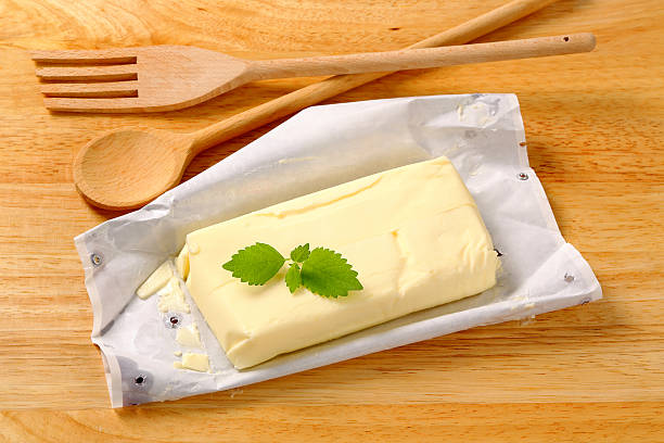 block of butter "block of fresh butter with a mint on a wrapping paper, wooden spoon and fork on a cutting board" butter margarine isolated portion stock pictures, royalty-free photos & images