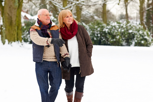 Image of happy mature couple in warm clothing walking outdoors in snow