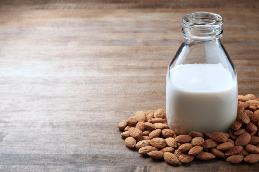 A bottle of almond milk surrounded by almonds.