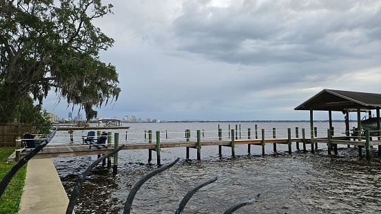 View of the St. Johns River in Jacksonville, FL with pier and cloudy sky. Includes far away view of Jacksonville skyline.