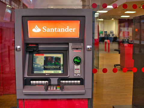 An automated teller machine (ATM) outside a branch of Santander in the UK. The interior of the bank is visible in the background.