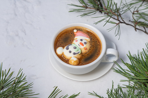 Cup of coffee with marshmallows. Marshmallow snowman in a Santa Claus hat. Winter drink in the snow. Christmas tree. Top view