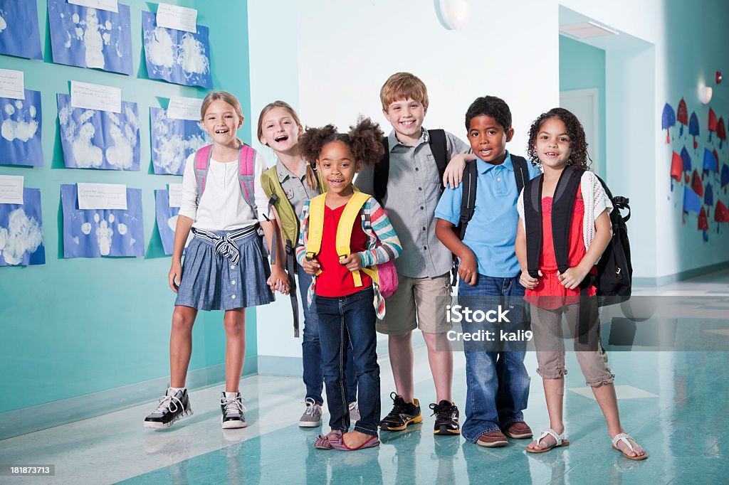 Children in school hallway Multi-ethnic children standing in hallway of elementary school carrying book bags. Child Stock Photo