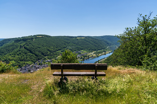 Lasserg, Rhineland-Palatine, Germany - June 14, 2021: A bench with a view at the River Moselle and the town of Burgen