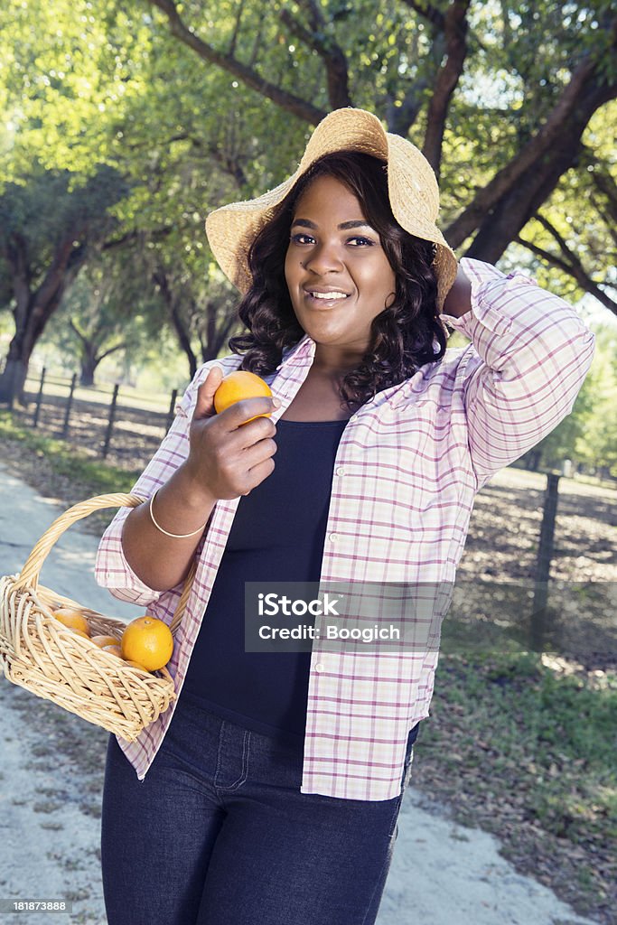 Black Woman with Basket of Florida Oranges "This is a vertical, color photograph of a black woman carrying a basket of Florida oranges as she walks down a rural dirt road." Adult Stock Photo