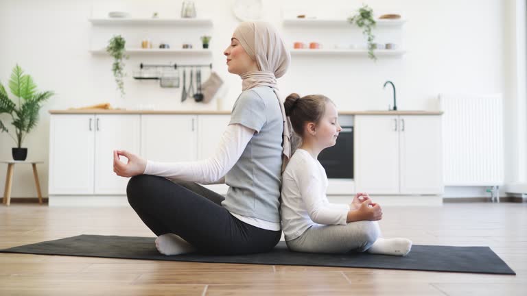 Mother promoting daughter's sense of calmness by meditating together at home.