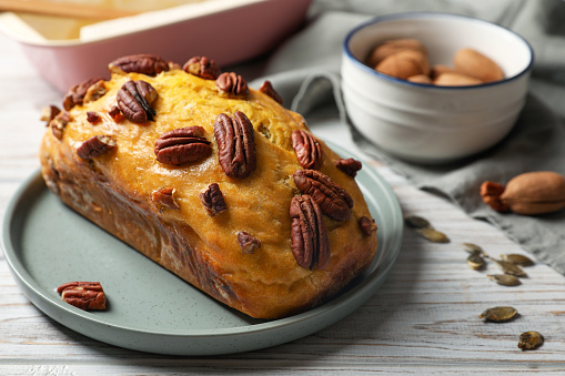 Delicious pumpkin bread with pecan nuts on light wooden table, closeup