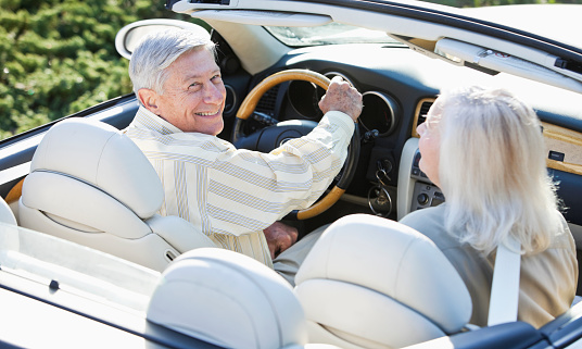 Senior couple (60s, 70s) having fun driving convertible.  Focus on man.