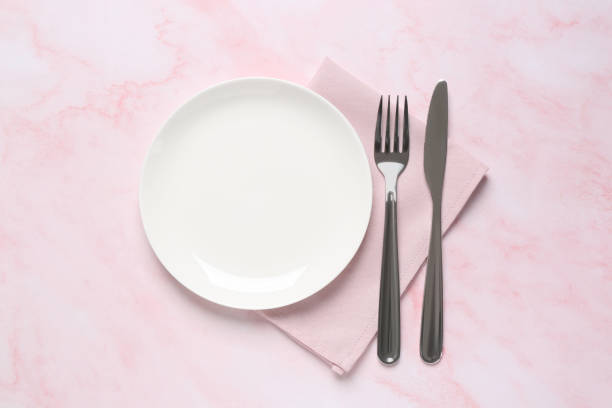 istock Clean plate and shiny silver cutlery on light pink marble table, flat lay 1818774512