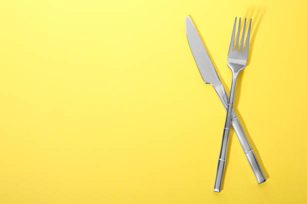 istock Shiny fork and knife on yellow background, flat lay. Space for text 1818775599