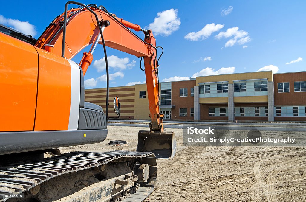 Excavator by New High School A bright orange construction excavator in the recently graded parking lot of a new high school.Similar Images: School Building Stock Photo