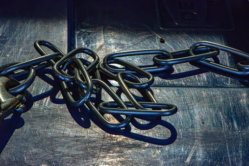 Close-up of a disorderly chain of steel in the shadows, with elongated links, on a scratched silver metal plate. Conveys a sense of cold, sadness, and darkness