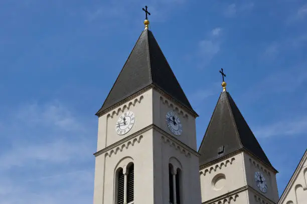 church clock tower with white round clock. stucco exterior wall. arched windows. steep Zink plate roof. twelve o`clock PM shown. roman numerals. the St Michael cathedral in Veszprem, Hungary