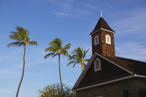 Small Christian coral church on the island of Maui juxtaposed against a brilliant azure blue sky and coco palms.