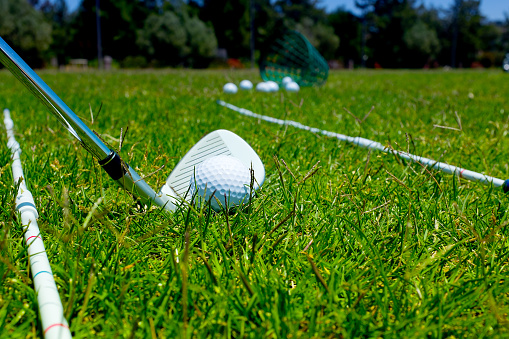 Photograph of a golf club, golf ball, and alignment aids on a driving range. This image uses a shallow depth of field with the focus on the golf ball.