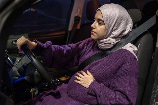 Pregnant arabic muslim woman driving car at night wearing winter clothes ,hijab and seat belt driving in confidently and feeling safe
