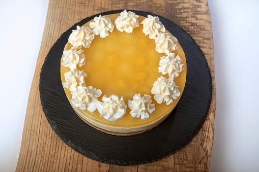 Lemon cheesecake cake decorated with whipped cream.\nCheese cream and yellow lemon glaze on a wood and slate tray.