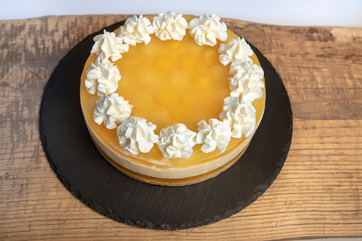 Lemon cheesecake cake decorated with whipped cream.\nCheese cream and yellow lemon glaze on a wood and slate tray.