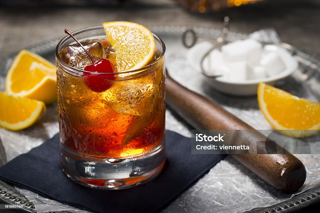 Old Fashioned Cocktail in a Vintage Bar "The Old Fashioned is most commonly made by muddling sugar cubes with bitters, a cherry and an orange wedge or peel. Usually a splash of water or soda water is added along with ice, bourbon (or rye) and a garnish." Cocktail Stock Photo