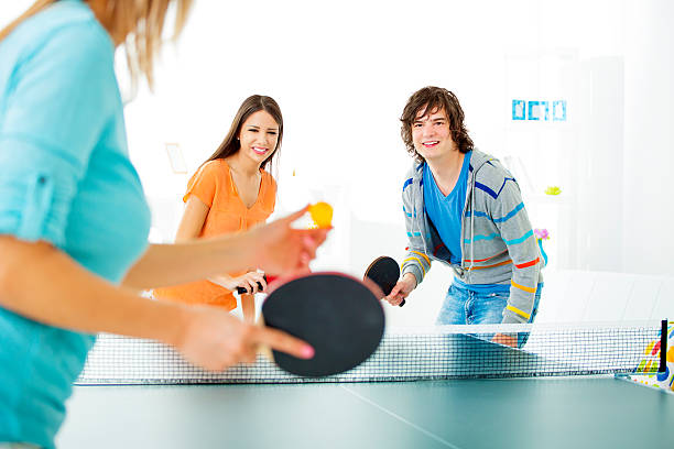 Young cheerful people playing table tennis at home, selective focus to couple waiting for other to serve table tennis ball.
