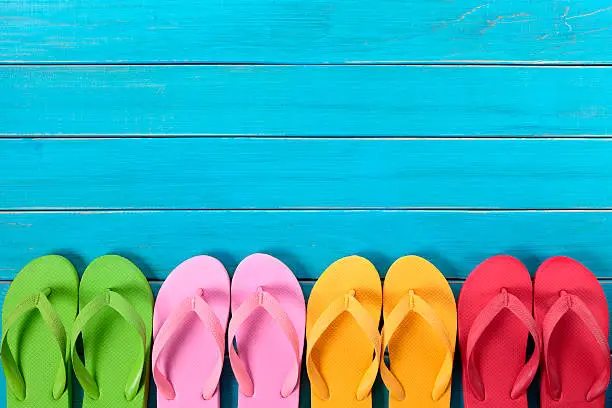 Row of colorful flip flops on old weathered blue painted beach decking.  Space for copy. You might also like the isolated on white version shown below:
