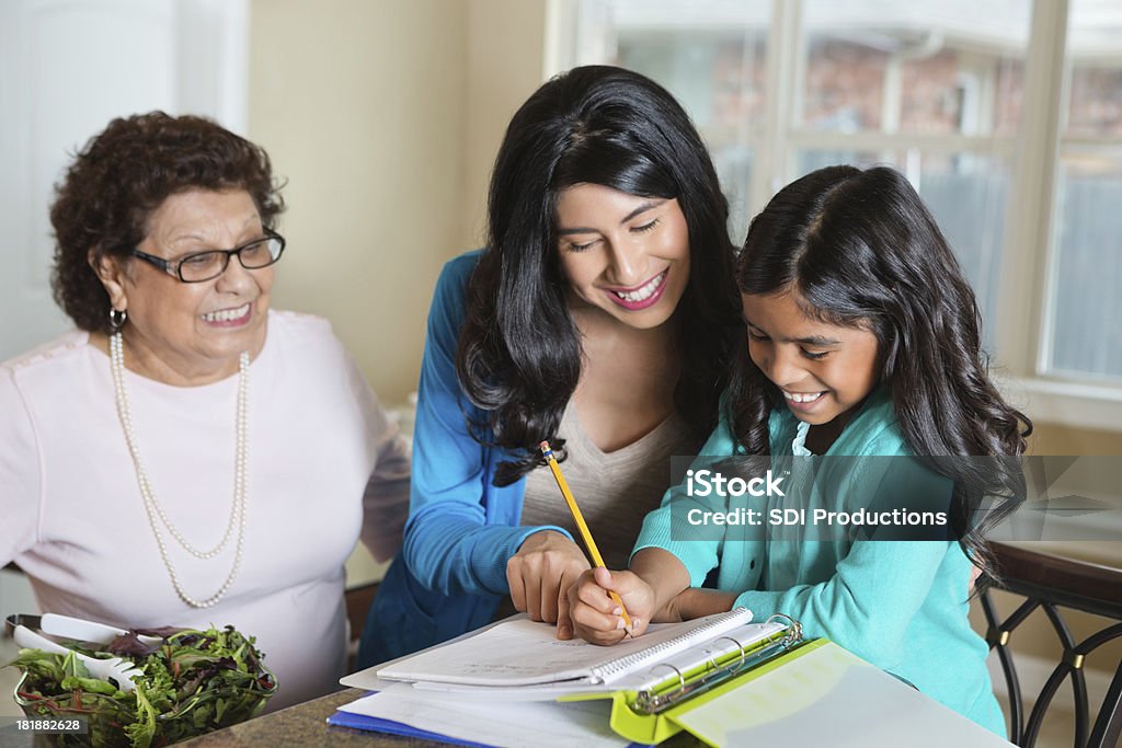 Ispaniche madre e nonna aiutando bambina con compiti a casa - Foto stock royalty-free di Compito a casa