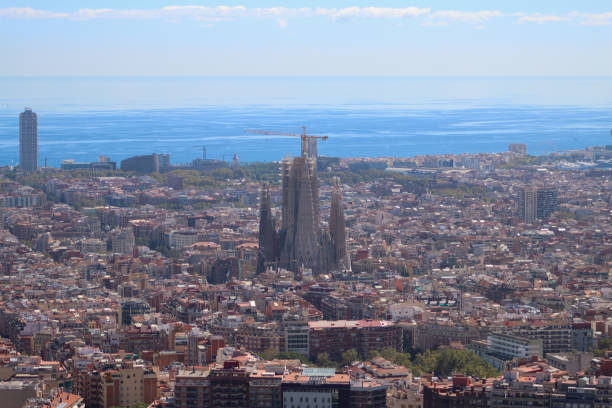 Barcelona, Spain - June 16, 2022:  Construction cranes complete the architectural details of the gothic Art Nouveau church spires of the Sagrada Familia basilica in the Eixample district of Barcelona Catalonia Spain as seen from the Gaudi Park pond