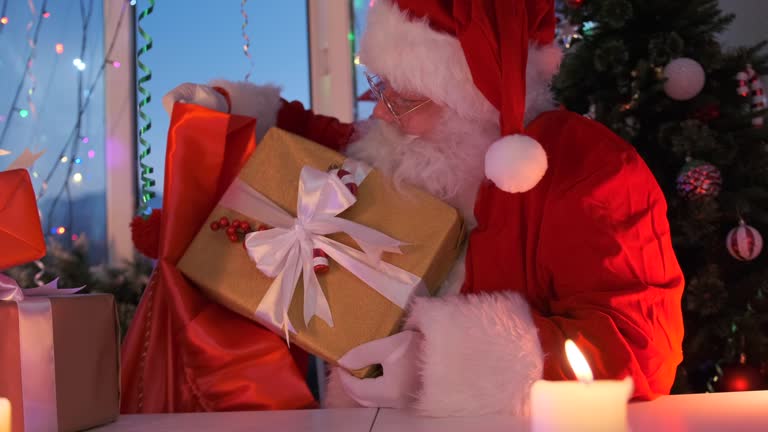 Santa with kind smile admires beautiful gift with white ribbon packed in craft paper puts it in present bag