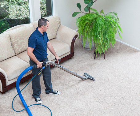 A close-up, low angle view of an unrecognizable cleaner using a professional vacuum cleaner to clean the carpets in an empty room.