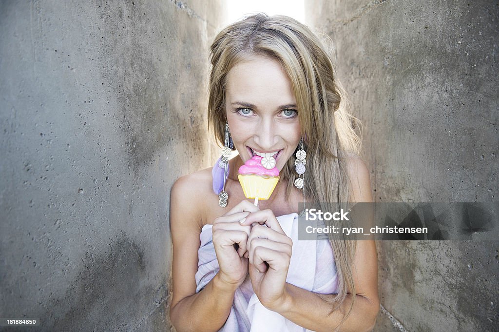 Belle jeune femme de ciment murs mâcher un Cupcake Sucker - Photo de A la mode libre de droits