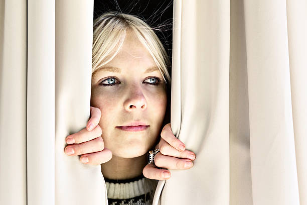istock Pretty blonde peeps sideways through closed curtains, smiling 181885871