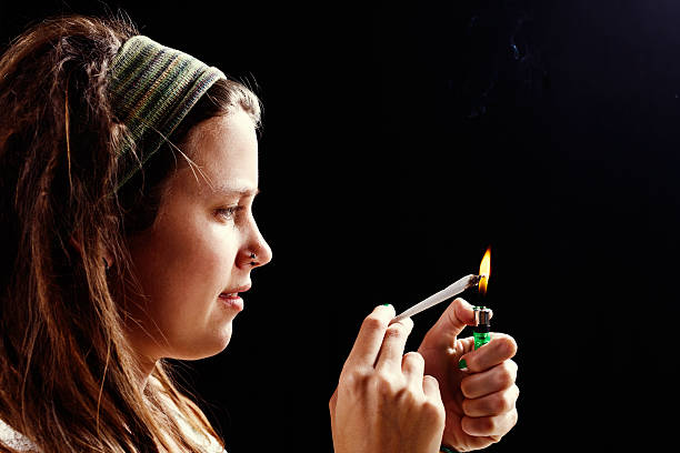 istock Young woman concentrating on lighting marijuana joint 181886142