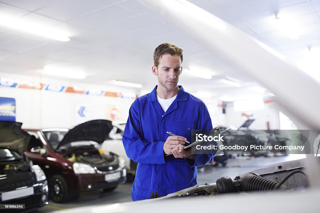 Could use a tune-up A handsome mechanic holding a clipboard and performing checks on a cars engine Adult Stock Photo