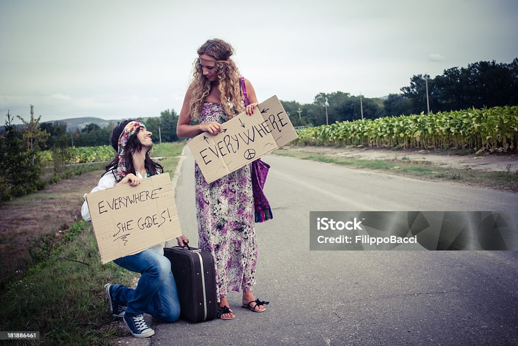 Young adult hippie couple hitchhiking with placards in hand Young adult hippie couple hitchhiking with placards in hand. Love concept. He's in love with her. 1960-1969 Stock Photo